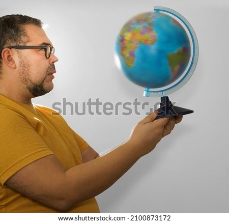 Young caucasian bearded geography student traveler indignant man in yellow basic t-shirt hold in hands Earth world globe. Male looking at globe map isolated on grey background. studio shot. 