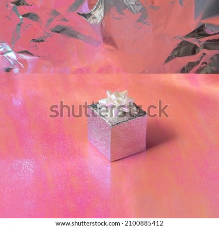 Modern party concept. Sparkling silver gift on orange and pink background. Minimalistic birthday celebration idea.