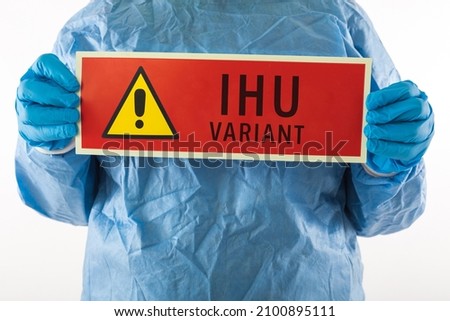 Detail of an arm of a medical nurse wearing a PPE and latex gloves with a red sign with a danger symbol that reads: ''IHU VARIANT''. Coronavirus, pandemic and health concept.