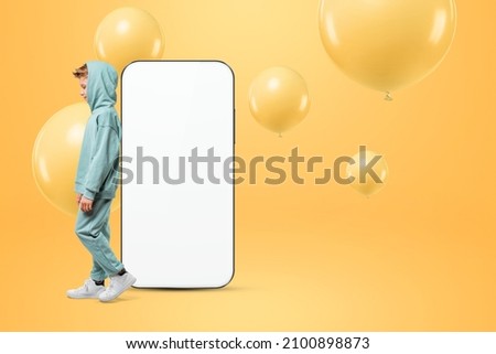 The boy is standing near a large smartphone with a white screen. Copy space, mixed media, ad layout, empty design environment, creative background