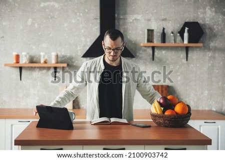 Front view of a business man working at home in kitchen. Smart working with tablets and notebook during the covid pandemic.