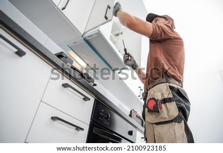 Residential Cabinetmaker Worker in His 40s Finishing New White and Modern Kitchen Cabinets Installation. Royalty-Free Stock Photo #2100923185