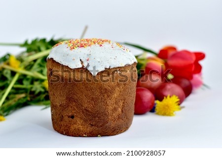 The picture shows a tall Easter cake with flowers lying nearby on a white background.