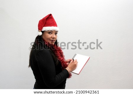 Latin adult woman with hat and Christmas garland shows banner and blank notebook to put a message of congratulations, love or wish list
