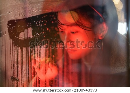 Sensitive asian millennial girl suffer from solitude alone draw on wet glass in rain. Unhappy young woman emotional and nostalgic after breakup with boyfriend feeling bad depression and loneliness