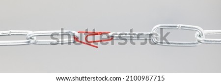 Chrome chain in middle with red paper clip. Broken chain linked by paper clip concept Royalty-Free Stock Photo #2100987715
