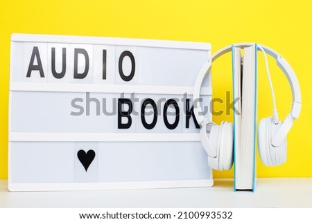 Audio book concept with modern white headphones and hardcover book on a yellow background. Listening to a book. E-learning. Copyspace. inscription on a lightbox
