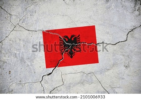 An old image of the flag of Albania on a wall with a crack. A crisis.