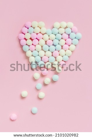 Pastel Pompoms heart dissolving into pieces on pink background flat lay. Valentines day, broken heart and love emergence concept top view. 