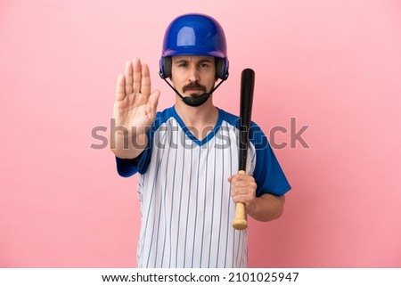 Young caucasian man playing baseball isolated on pink background making stop gesture