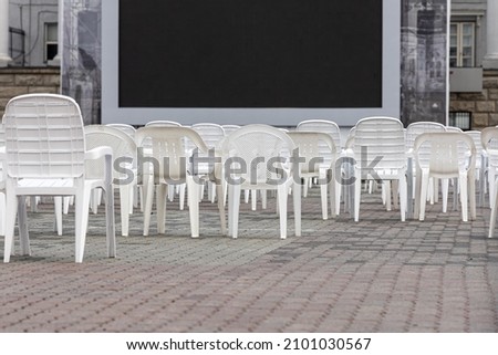 The Open air cinema with group of white plastic chairs and black screen in summer day without people