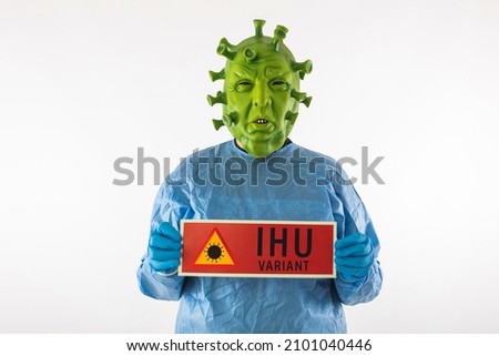 Man dressed in coronavirus latex mask, PPE and latex gloves, holding a red danger sign that reads: 'IHU variant', on white background. Coronavirus, health, pandemic, quarantine.