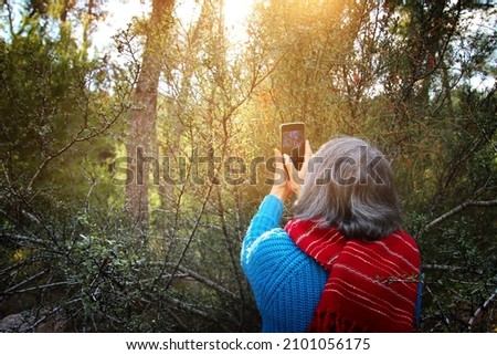 Back view of senior woman photographing nature during walk in the forest