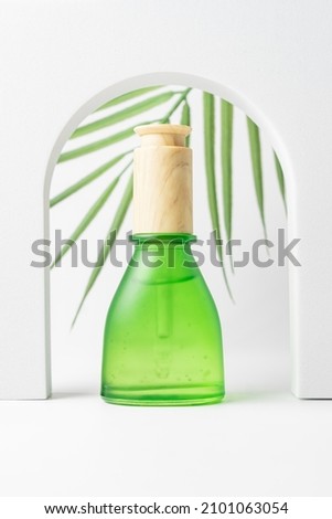 Green dropper bottle on white background with tropical palm leaf. Blank aromatic oil container design, medical packaging template. Herbal cosmetic concept. Trendy showcase with podium and greenery.