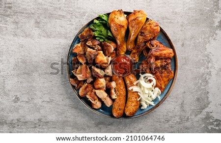Assorted grilled meat in a plate on the table top view. Fried chicken legs and wings, sausages, shish kebab, pickled onions and tomato sauce. Horizontal orientation, copy space, no people Royalty-Free Stock Photo #2101064746