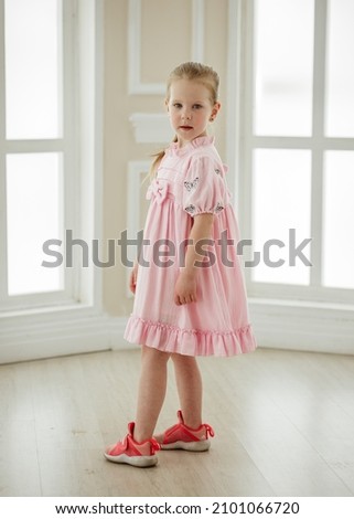 Light brown hair beautiful little girl in designer dress stands near the window indoor