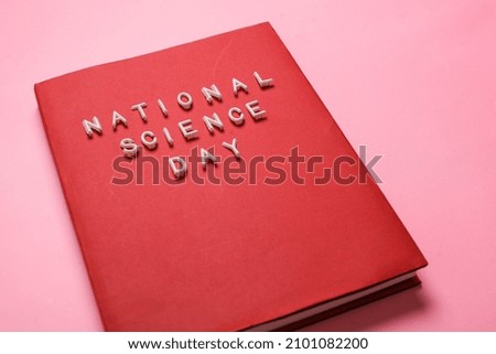 A red book with the words national science day isolated on a pink background