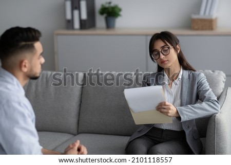 Psychotherapy concept. Focused female psychotherapist interviewing young man, listening and taking notes. Arab guy having session with professional female psychologist