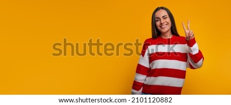 Charming smiling young modern woman shows victory sign while she posing isolated on yellow wall