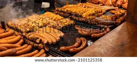Lots of tasty juicy meat, bbq, outdoors grill, sausages, shahlik, steam over hot grilled food, high resolution, wide shot, panoramic, warm colors. Traditional street food market stall closeup, nobody Royalty-Free Stock Photo #2101125358