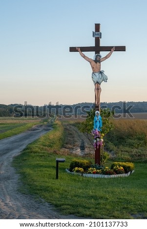A vertical shot of a wooden cross with the picture of Jesus Christ in a rural area