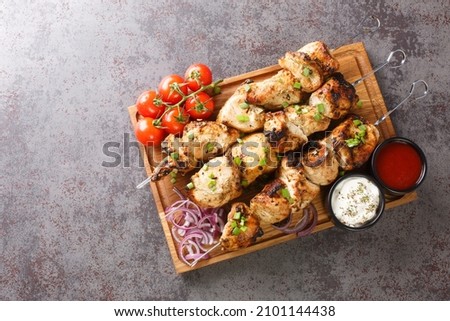 Juicy grilled chicken skewers with fresh vegetables and two sauces close-up on a wooden tray on a gray concrete background. horizontal top view from above Royalty-Free Stock Photo #2101144438
