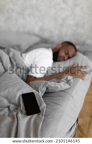 African American Man Sleeping, Resting In Bed At Home, Lying Near Smartphone, Vertical Portrait, Blurred Background, Selective Focus On Cell Phone With Black Blank Screen For Mock Up Template