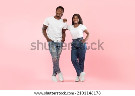 Confident People. Portrait of casual African American young couple standing at studio and posing, lady leaning on guy looking at camera isolated over pink wall, full body length, banner