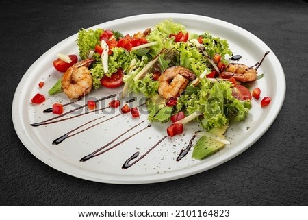 Salad with avocado and tiger prawns, seasoned with pesto sauce. Isolated on a black background.