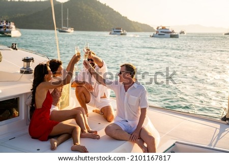 Group of man and woman friends enjoy party drinking champagne with talking together while catamaran boat sailing at summer sunset. Male and female relax outdoor lifestyle on tropical travel vacation Royalty-Free Stock Photo #2101167817