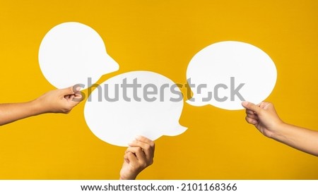 A speech bubble concept. Hand holding of an empty white speech bubble against a yellow background. Space for text. Close-up photo
