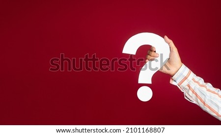 Question mark symbol concept. Hand holding a white question mark paper while standing on a red background in the studio. Close-up photo. Space for text