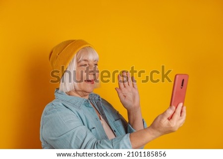 Portrait of 50s cheerful caucasian woman holning phone, having online conference good mood isolated over bright color background