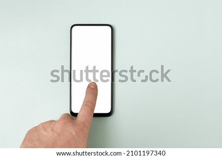 A smartphone with an empty white display, a finger touching the screen. With a place for the inscription. Blue-green pastel background.