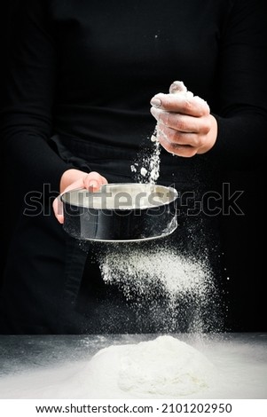 Sifting flour through a sieve. Flour in hands. On a dark background.