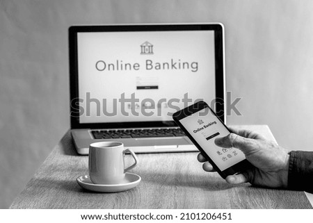 A male holding a phone with a writing online banking and a computer in the background