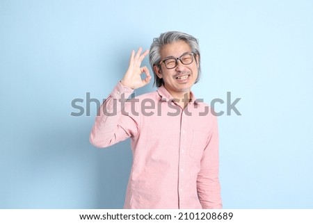 The senior Asian man standing on the blue background with pink shirt.