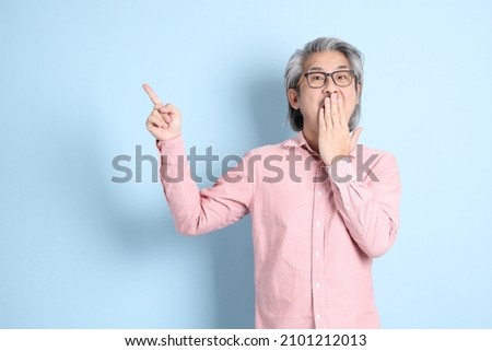 The senior Asian man standing on the blue background with pink shirt.