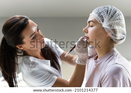 Professional permanent makeup artist and her client during lip blushing procedure Royalty-Free Stock Photo #2101214377