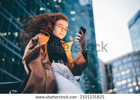Successful woman using smartphone outdoors while standing near skyscraper at night.  Royalty-Free Stock Photo #2101231825