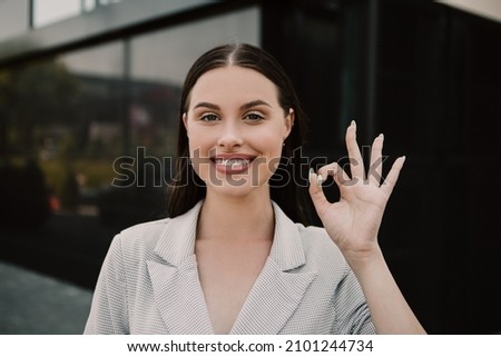 Small business owner office worker smiling happy woman standing outside building showing OK gesture sign. Female successful executive girl on the street. Copy space.