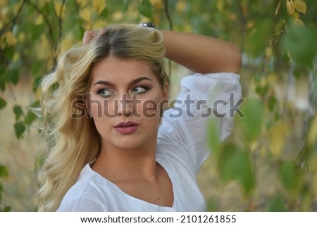 Beautiful young blonde girl in white shirt, surrounded by green forest.