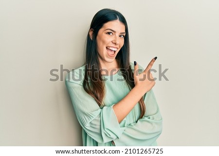 Young hispanic woman wearing casual clothes smiling cheerful pointing with hand and finger up to the side 