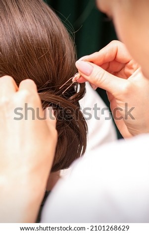 A hairdresser is making the hairstyle of a young brunette woman in a hair salon, close up.