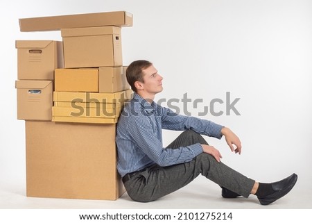 A man with many boxes. Boxes symbolize change of residence. Man is tired of moving to new home. Guy with boxes on white background. Guy is thinking about logistics of personal belongings Royalty-Free Stock Photo #2101275214