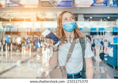 COVID-19 Happy blonde hair female tourist with a backpack in a protective medical mask with a passport while waiting for the passport check of the tourist at the airport Royalty-Free Stock Photo #2101275370
