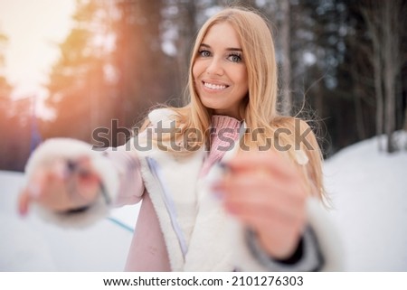 Winter fashion portrait of young happy blonde woman holding glasses for vision on background of forest and snow.