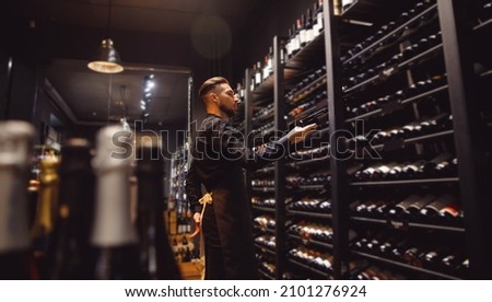 Sommelier Bartender man at wine shop full of bottles with alcohol drinks. Royalty-Free Stock Photo #2101276924