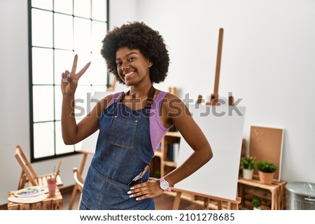 Young african american woman with afro hair at art studio smiling looking to the camera showing fingers doing victory sign. number two. 