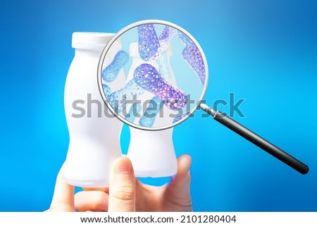 Probiotic yogurt. Magnifying glass with probiotic molecules. Jars with probiotic yogurt on blue. Concept of fermented milk products with beneficial microorganisms. Microbiome research. Royalty-Free Stock Photo #2101280404